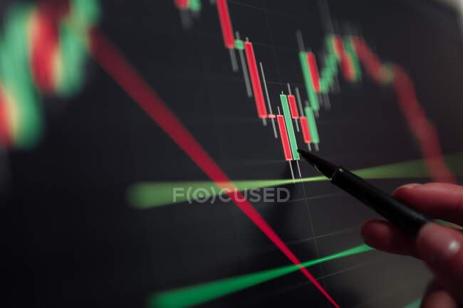Crop unrecognizable broker pointing at display with binary option while working with graphics — Stock Photo
