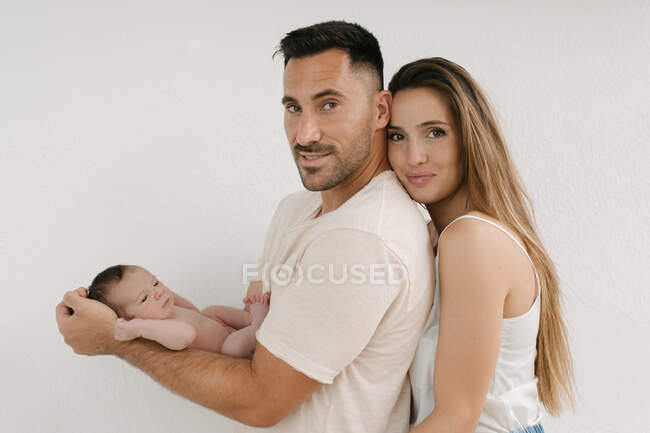 Vista lateral do casal encantado com bebê nu olhando para a câmera no fundo branco — Fotografia de Stock