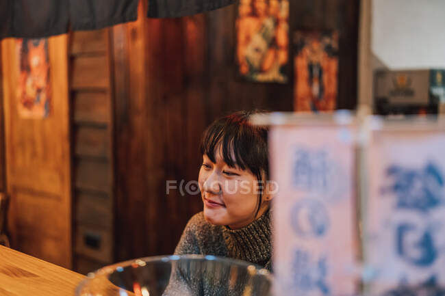 Азиатка в повседневной одежде сидит за деревянным столиком, ожидая заказа в рамен-баре — стоковое фото