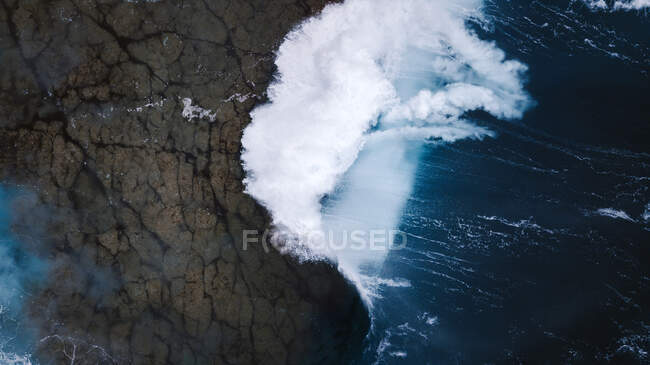 Drone view of breathtaking scenery of foamy sea waves crashing on rough rocky seashore — Stock Photo