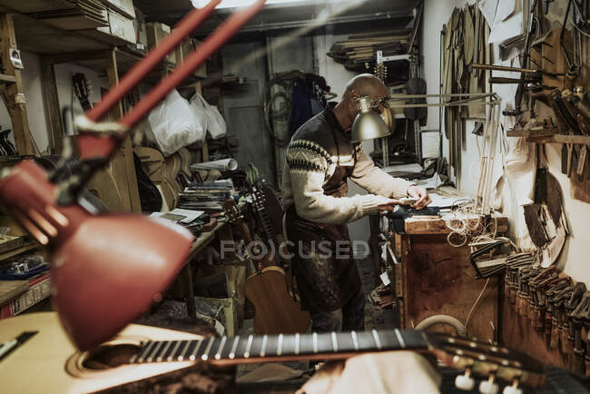 Side view of unrecognizable bald male artisan repairing instruments at workbench in small art studio near acoustic guitars and various tools — Stock Photo