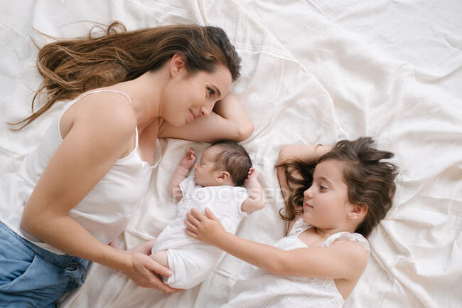 Desde arriba de la madre sonriente y la niña acostada en la cama con un bebé lindo - foto de stock