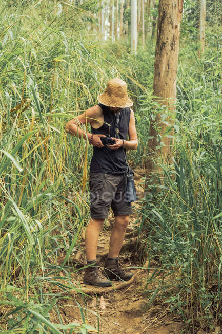 Viajando fotógrafo masculino tomando fotos en cámara fotográfica durante la aventura de verano en el bosque - foto de stock