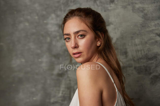 Side view of attractive female with long hair looking at camera on gray background in studio — Stock Photo