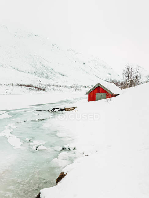 Cabaña roja situada a orillas del río nevado blanco en las Islas Lofoten, Noruega - foto de stock