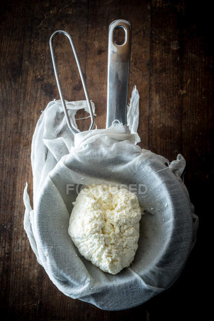 Top view of fresh homemade cottage cheese in colander with cloth placed on wooden table — Stock Photo