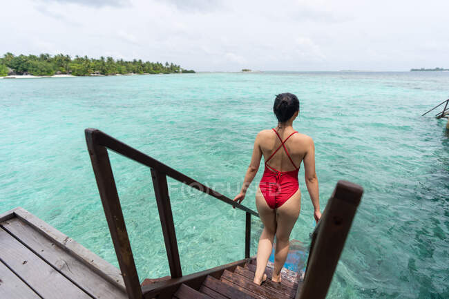 Rückenansicht einer anonymen Frau im Badeanzug, die auf den Malediven eine Treppe ins Wasser hinuntersteigt und sich entspannt — Stockfoto