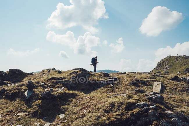 Vista posterior de un excursionista masculino distante irreconocible con mochila de pie en una colina rocosa en las tierras altas durante el trekking en Gales - foto de stock