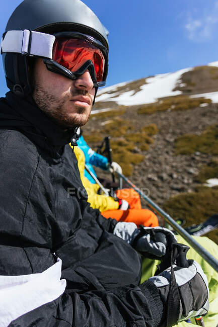 Bearded male athlete in sports glasses and helmet admiring winter mountain against anonymous partners on sunny day in Spain — Stock Photo