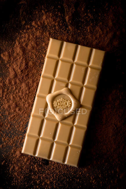 From above of whole chocolate bar with love inscription served on black background with scattered cocoa powder — Stock Photo