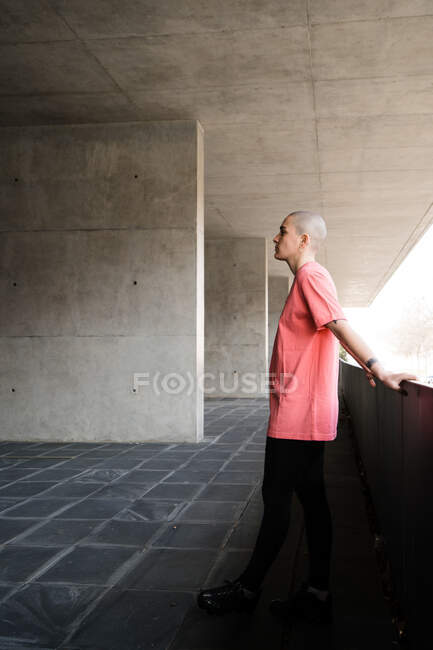 Side view of transgender person in t shirt standing looking away against fence in masonry construction in daytime — Stock Photo