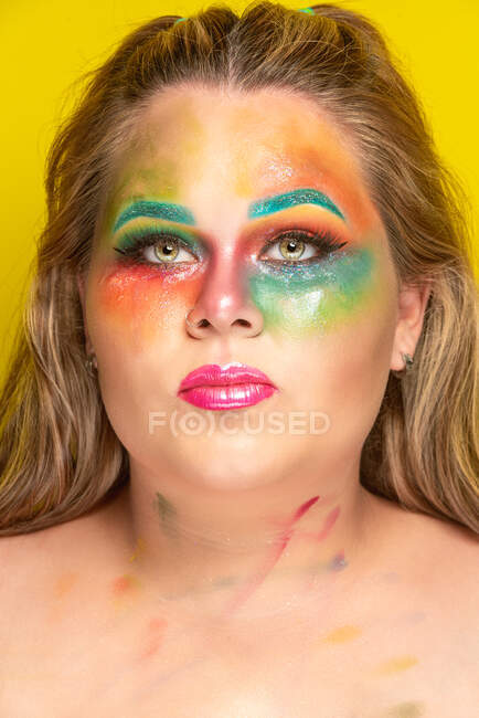 Plus size female with bright colorful makeup looking at camera against yellow background — Stock Photo
