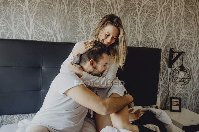 Веселий молодий чоловік і жінка посміхаються і качаються, сидячи на зручному ліжку вдома разом — стокове фото