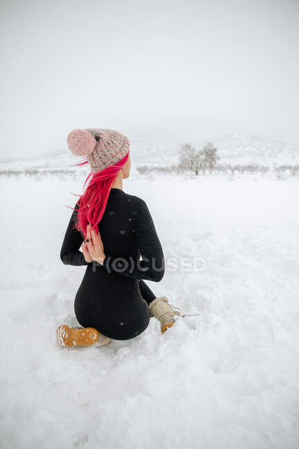 Задній вигляд гнучкої самиці з рожевим волоссям сидить у Гомухасані з руками Намасте позаду і практикує йогу на сніговій лузі взимку. — стокове фото