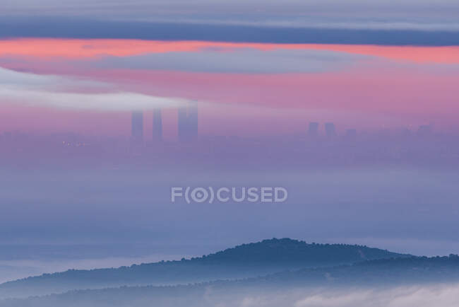 Aerial view of modern skyscrapers of Cuatro Torres in madrid and mountains covered with tick clouds under colorful sky during sunrise — Stock Photo