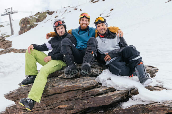 Cheerful male athletes in goggles embracing on rough mount with snow in province of Granada Spain — Stock Photo
