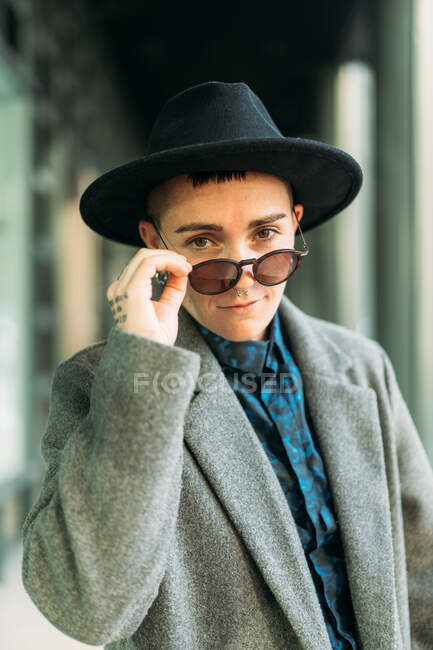 Young transgender person in classy coat and hat looking at camera in daylight — Stock Photo