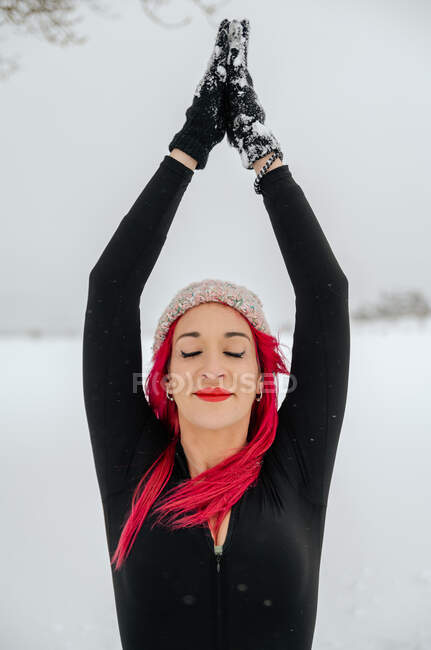 Content female with pink hair practicing yoga in Gomukhasana while sitting with Namaste gesture in snowy winter field — Stock Photo