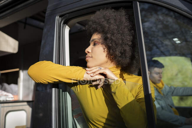 Excited African American female traveler smiling and taking selfie while peeking out from window of van near boyfriend — Stock Photo