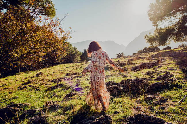 Visão traseira da fêmea despreocupada no vestido de verão em pé na colina rochosa nas terras altas no dia ensolarado — Fotografia de Stock