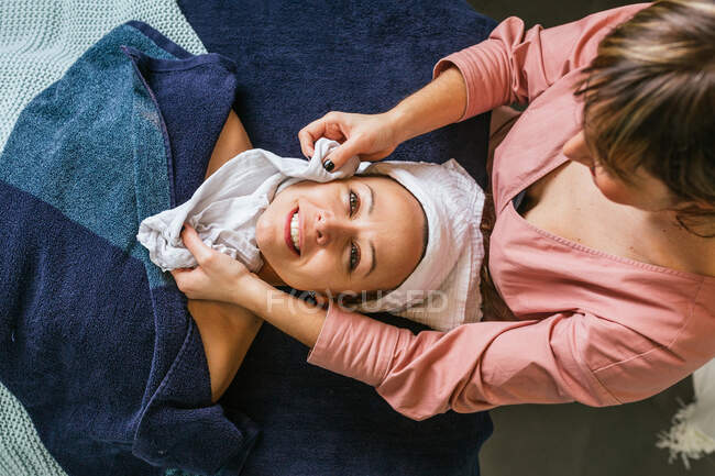 Vista dall'alto dell'estetista che pulisce il viso del cliente femminile con asciugamano durante la routine di cura della pelle nel salone spa — Foto stock