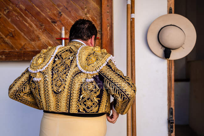 Vue arrière du picador anonyme se préparant pour la corrida revêtant un costume brillant traditionnel dans une écurie — Photo de stock