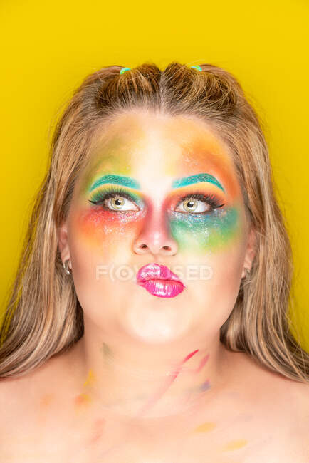 Плюс размер женщины с ярким цветным макияжем, отводящим взгляд на желтом фоне — стоковое фото