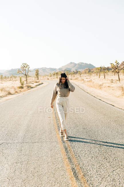 Полное тело брюнетки, идущей по пустой дороге в горячей местности национального парка Джошуа Три в Калифорнии — стоковое фото