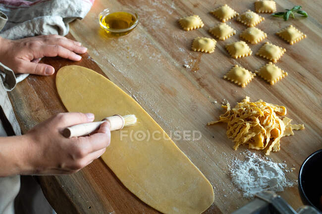 Unrecognizable person preparing raviolis and pasta at home. She is painting the pasta with eggs — Stock Photo