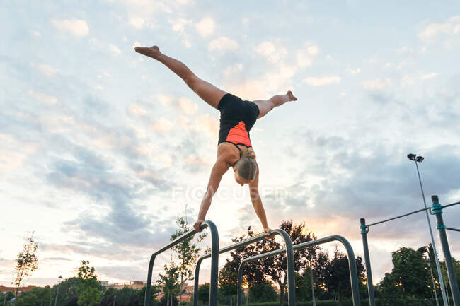 Снизу неузнаваемая спортсменка делает стойку на руках на параллельных брусьях в парке на фоне голубого неба — стоковое фото