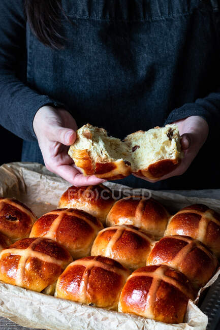 Bollos cruzados calientes recién horneados de la abertura del panadero femenino en bandeja para hornear - foto de stock