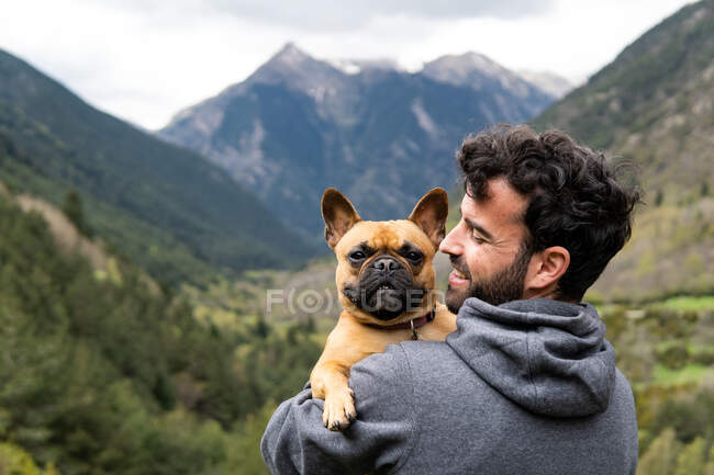 Back view of content male hiker sitting on rock embracing French Bulldog during adventure in Pyrenees mountain range — Stock Photo