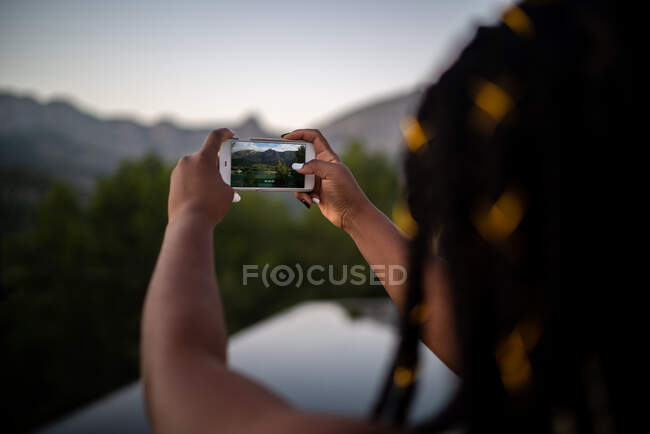 Récolte méconnaissable voyageuse afro-américaine prenant des photos sur smartphone de l'étang dans les hautes terres — Photo de stock