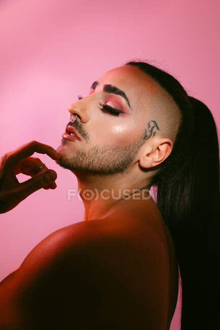 Vista laterale ritratto di glamour transgender donna barbuta in sofisticato make up posa contro sfondo rosa in studio — Foto stock