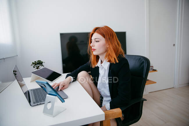 Вид збоку молодої жінки-підприємця, що працює на нетбуці за столом з планшетом і смартфоном вдома — стокове фото