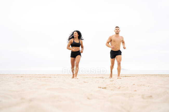 Nivel del suelo de diversas deportistas y deportistas que corren en la costa arenosa durante el entrenamiento de fitness en verano - foto de stock