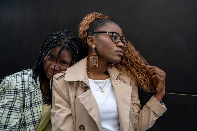 Sanfte Afroamerikanerin lehnt sich an beste Freundin und berührt lockiges Haar an schwarze Wand — Stockfoto