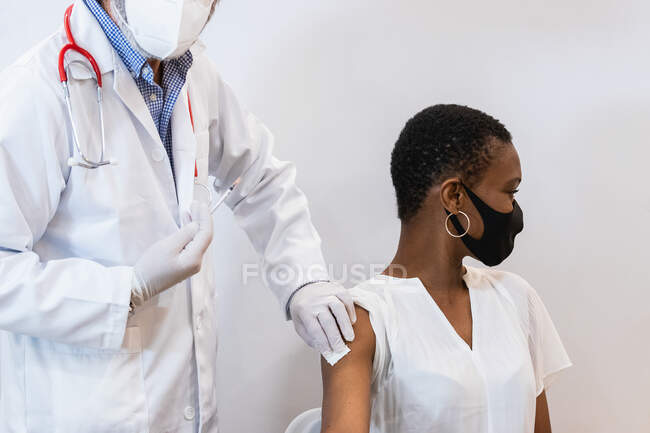 Cultiver mâle medic faire injection pour noir femme patient dans masque — Photo de stock
