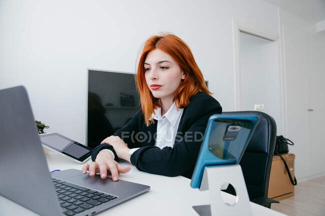 Jovem empresária trabalhando no netbook na mesa com tablet e smartphone em casa — Fotografia de Stock