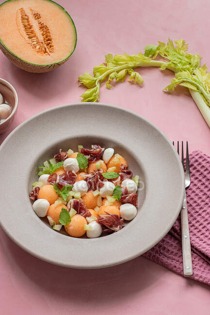 Dall'alto melone esotico, mozzarella e insalata di prosciutto su sfondo rosa colorato — Foto stock