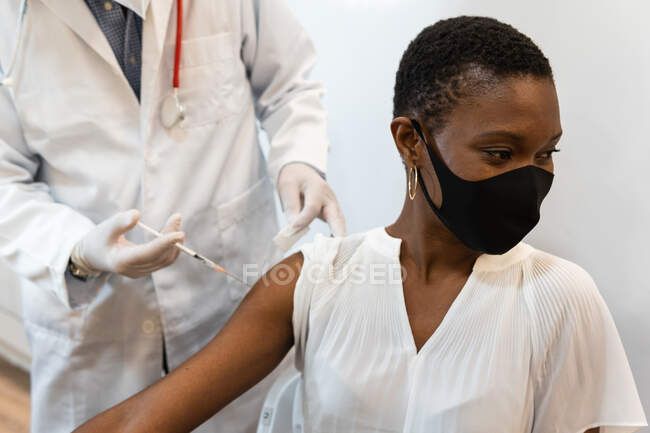 Colheita médica masculina fazendo injeção para paciente feminino preto em máscara — Fotografia de Stock