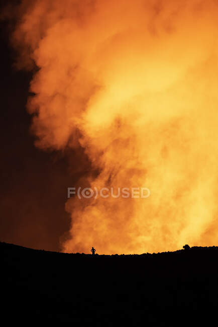 Silhouette di viaggiatore anonimo in piedi contro il fumo arancione del vulcano attivo in Islanda — Foto stock