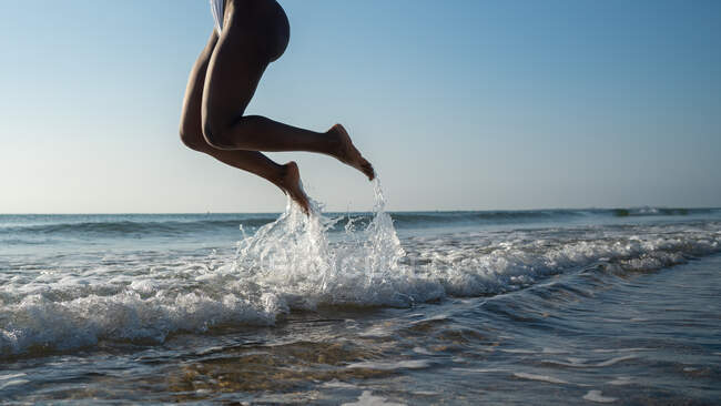 Vista lateral anónima mujer negra saltando en la playa - foto de stock
