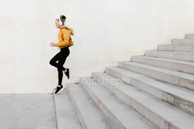 Молодая атлетичная белая женщина в наушниках и спортивном костюме, бегает по лестнице на улице — стоковое фото