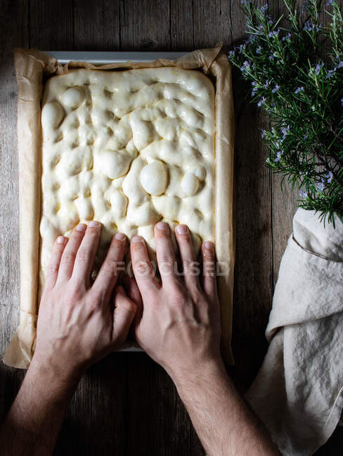 Вид зверху на безлику людину, яка готує сире тісто для хліба, розміщеного на папері для випічки на столі — стокове фото