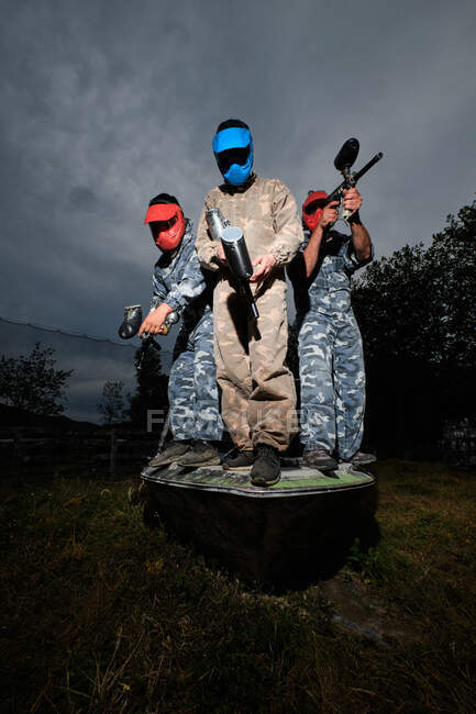 Angle bas des équipes de joueurs de paintball en tenue de camouflage et avec des fusils sur fond de ciel nuageux en soirée — Photo de stock