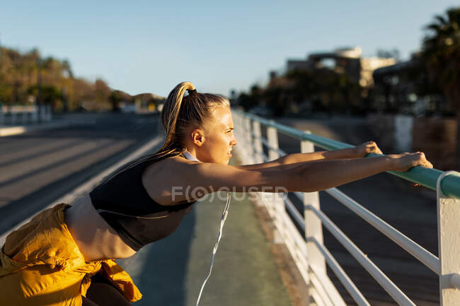 Young athletic caucasian leaning on banister stretching outdoors near road — Stock Photo