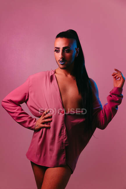 Ritratto di donna barbuta transgender glamour in sofisticato make up posa con le mani in vita contro sfondo rosa in studio guardando altrove — Foto stock