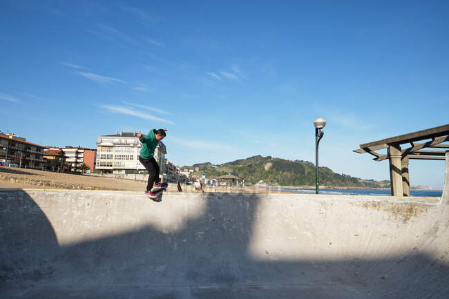 Unrecognizable man riding skateboard in skate park on sunny day on seashore — Stock Photo