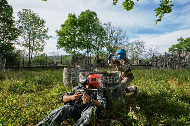 Joueurs d'équipe méconnaissables en tenue de camouflage et avec des fusils pointant les uns vers les autres tout en jouant au paintball — Photo de stock